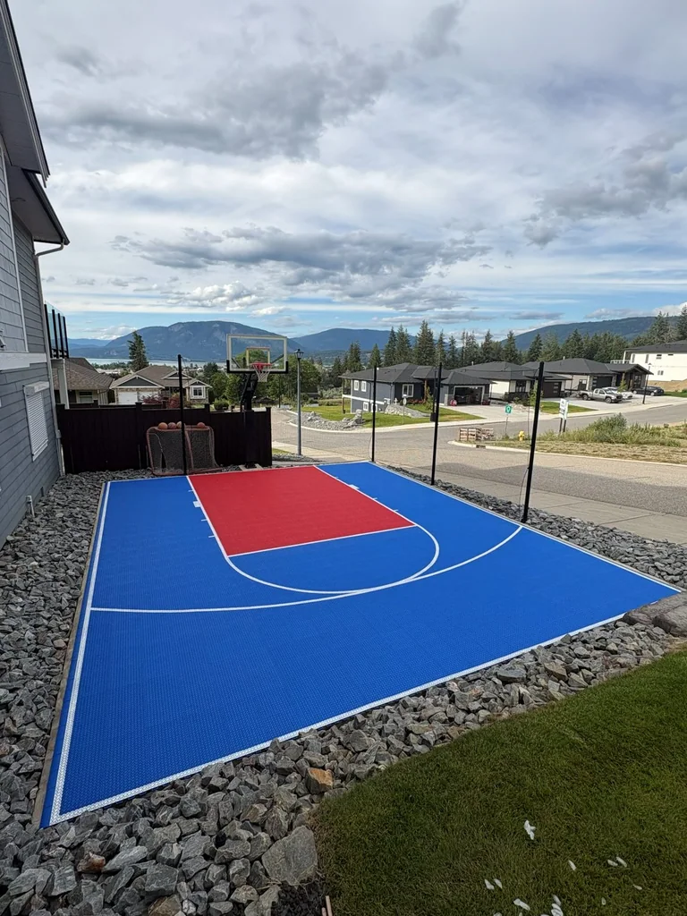 Completed blue and red basketball court beside a house with a lake view