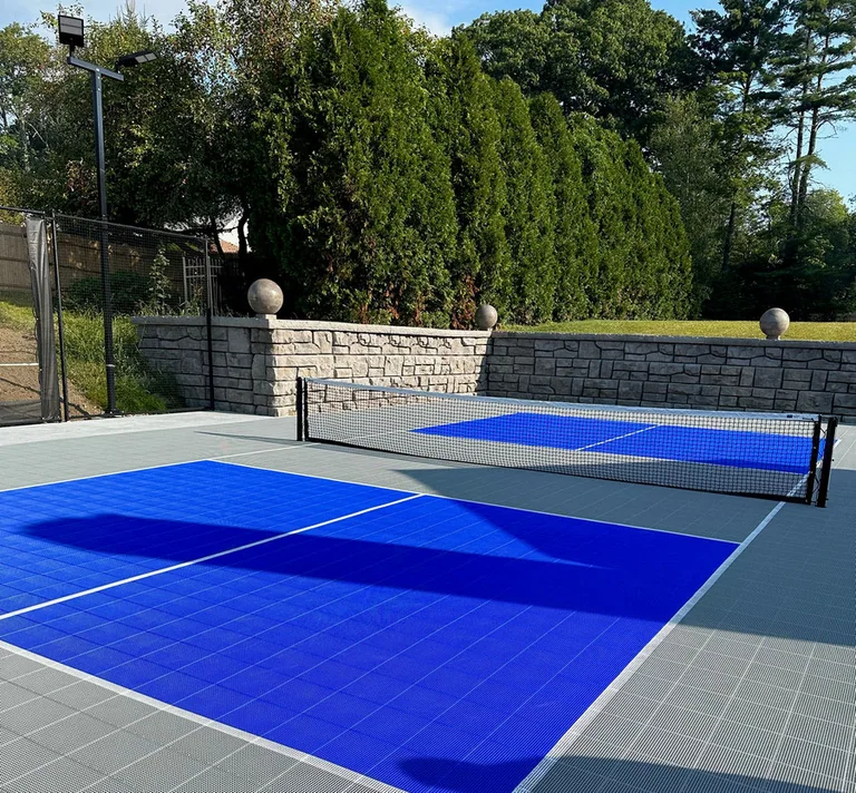 Outdoor pickleball court in blue and grey tiles against a stone wall